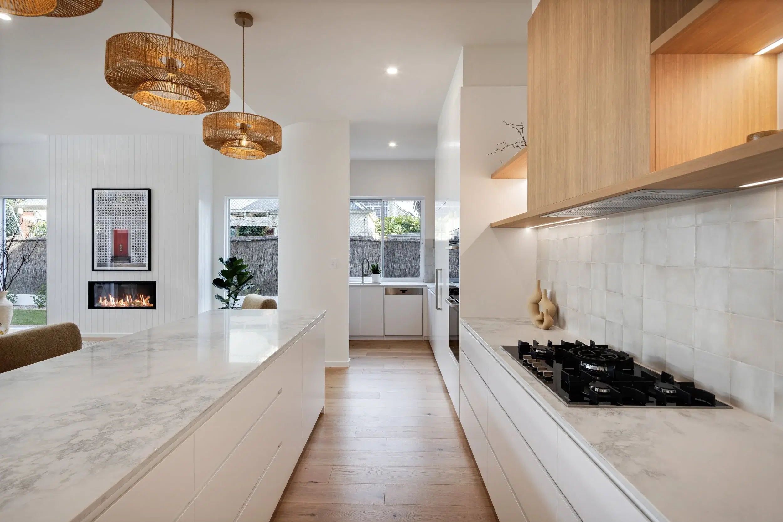 Warm timber and white kitchen with stone island and woven pendant lights