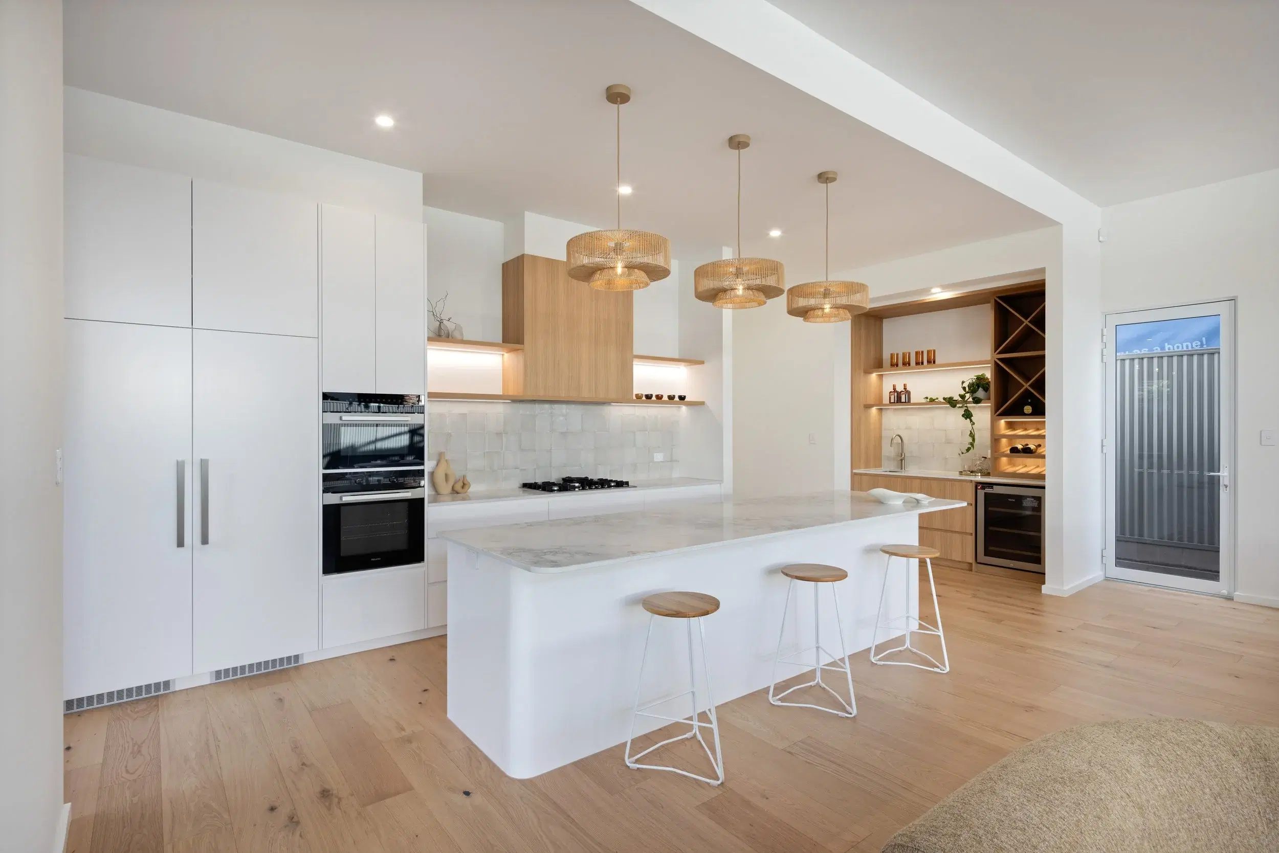 Open kitchen with pale stone island, timber cabinetry and woven lights