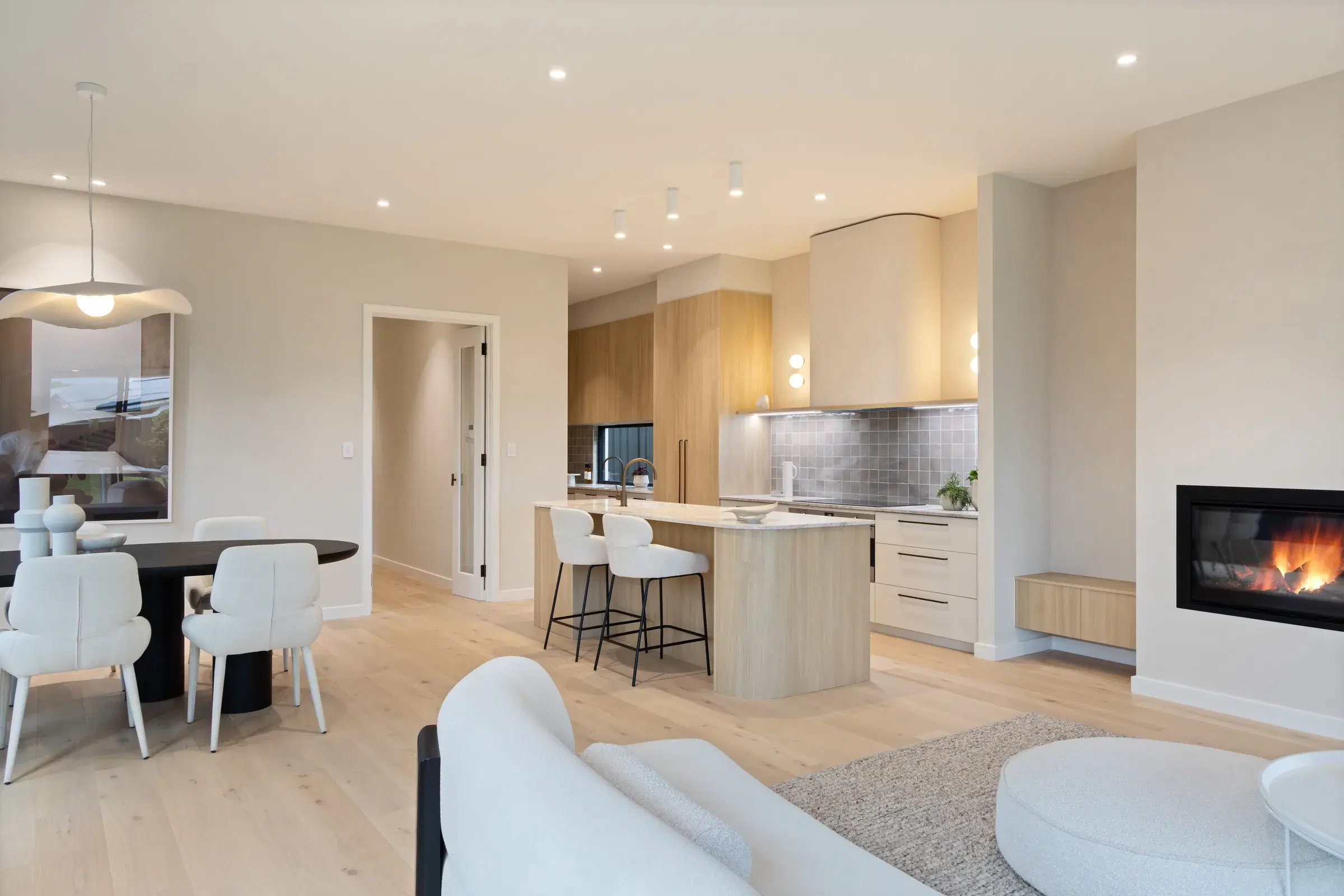 Open living and kitchen interior with pale timber cabinetry and fireplace