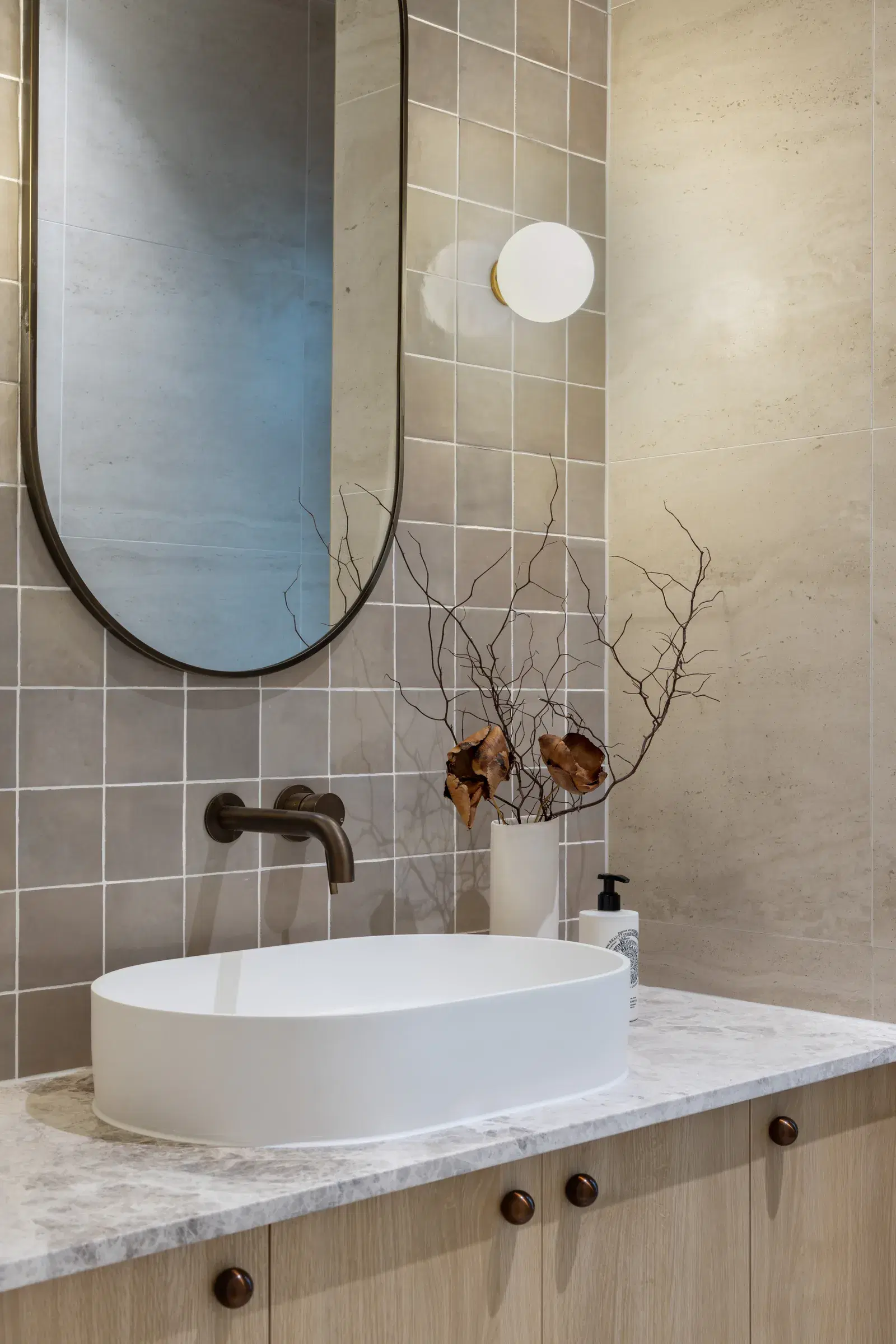 Pale timber bathroom vanity beneath an oval mirror and globe lights