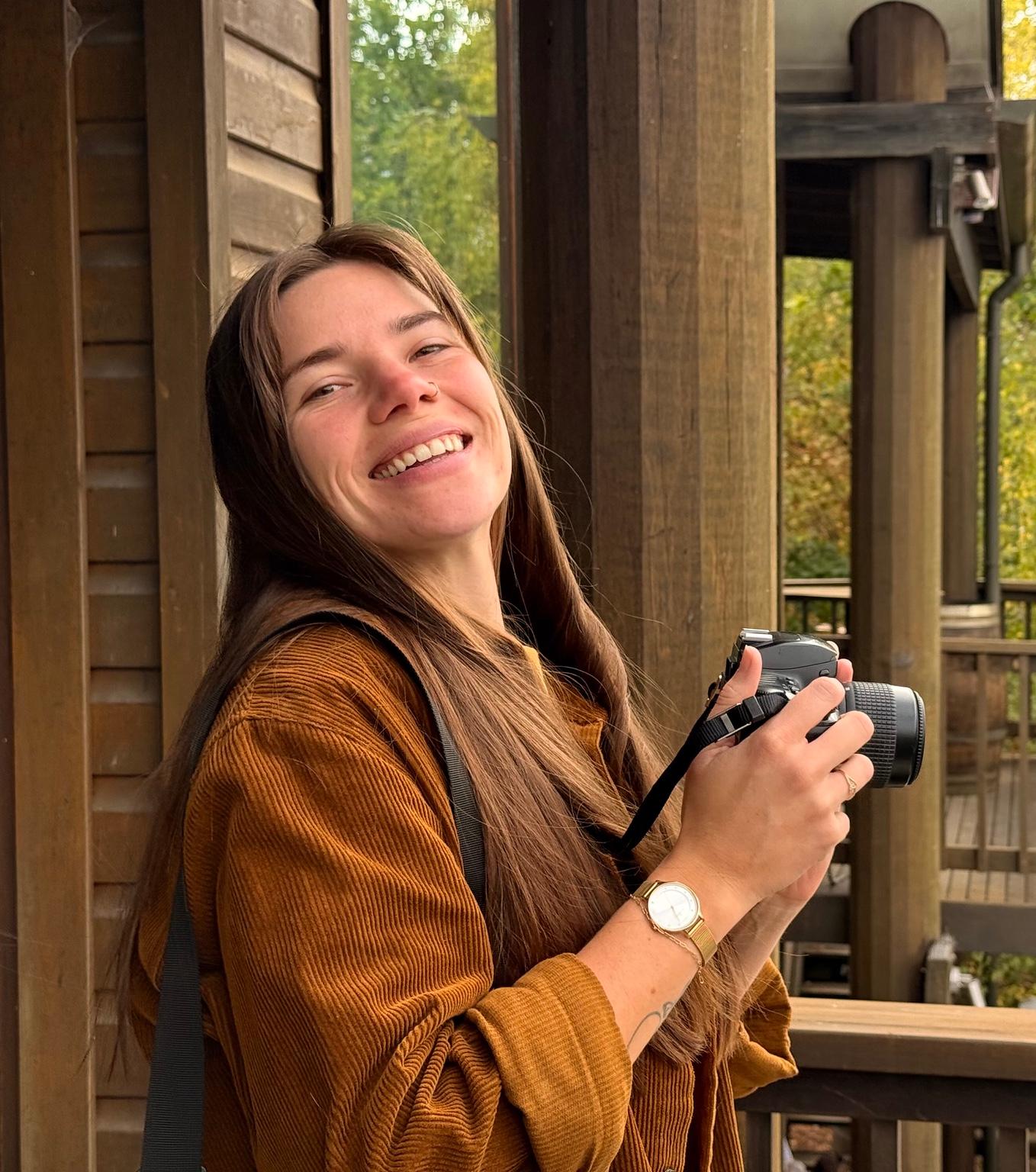 Saba smiling while holding a camera in a timber setting