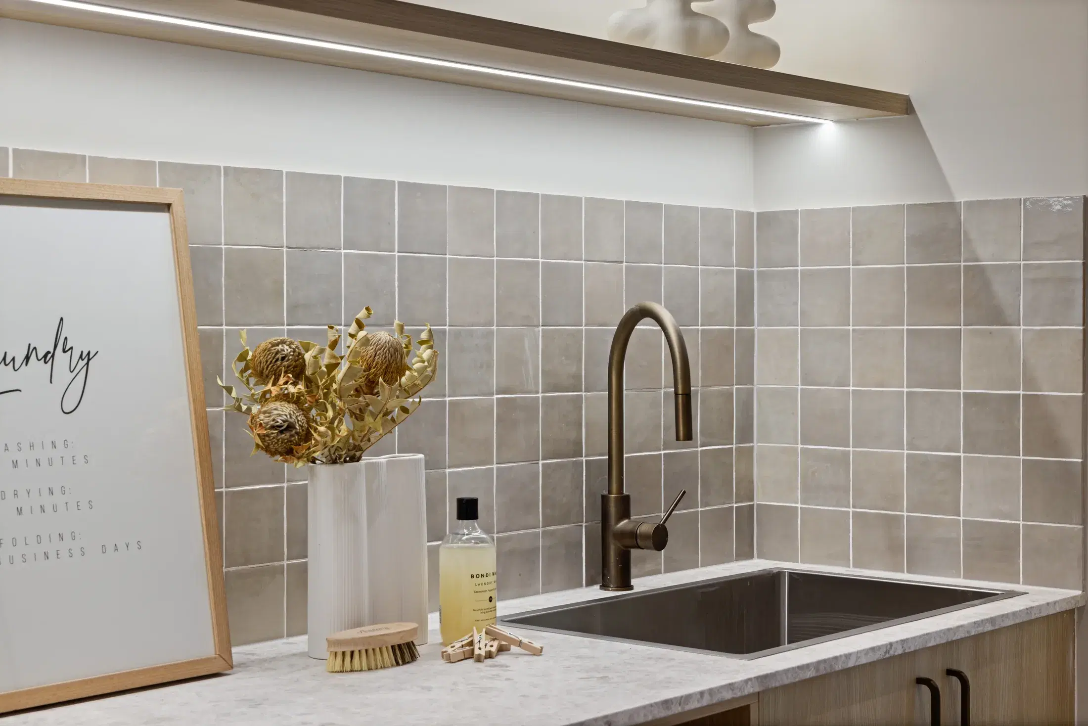 Laundry sink detail with square tiled splashback and bronze tap