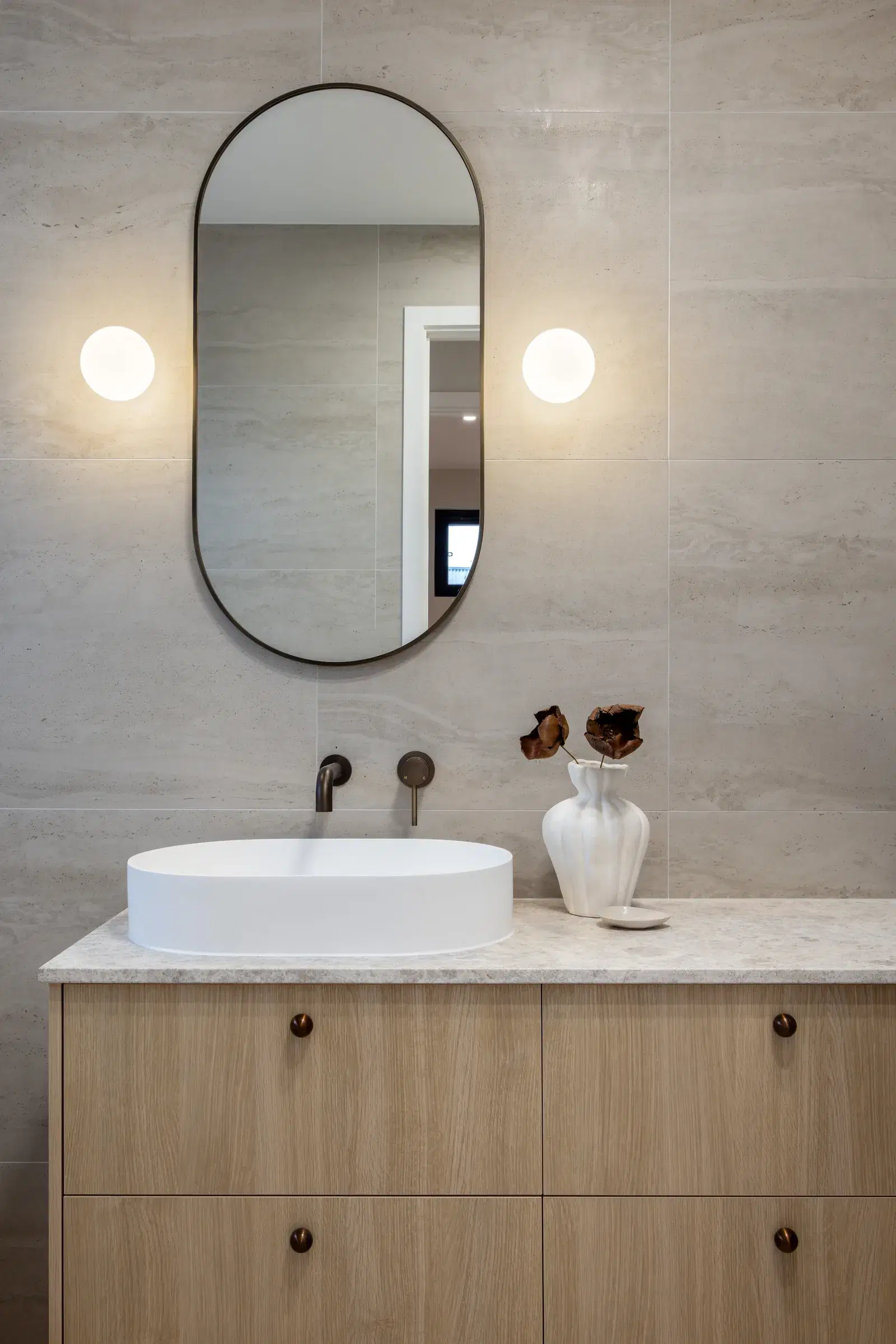 Bathroom vanity with oval mirror, globe wall lights and pale timber cabinetry